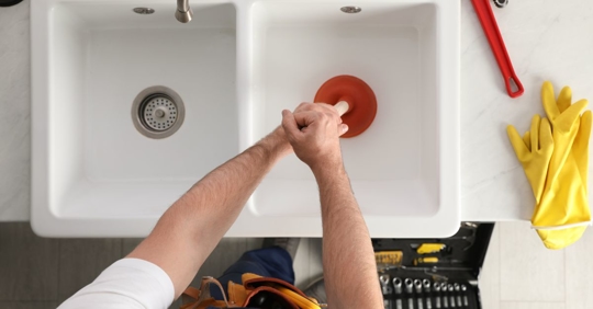 man unclogging drain with plunger